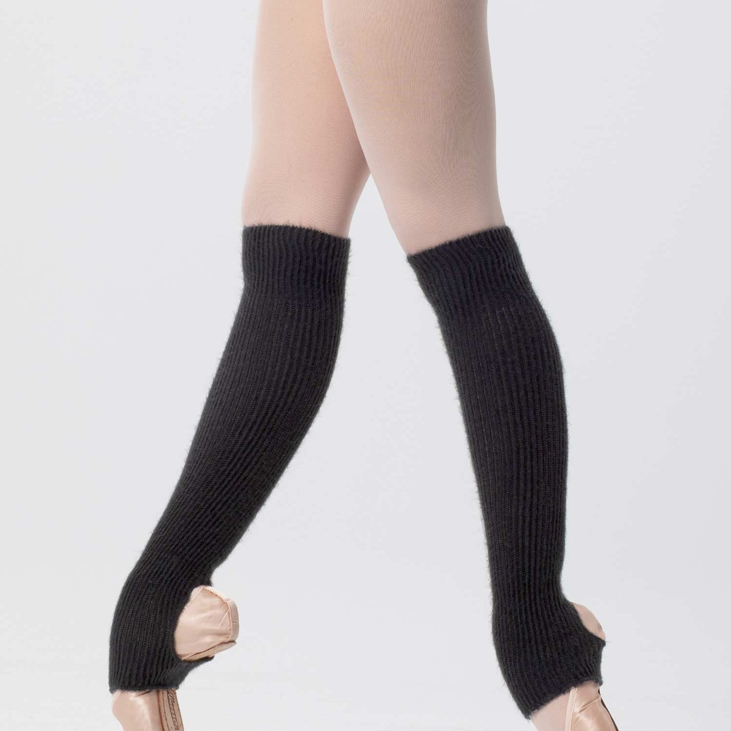 Eine Balletttänzerin steht in rosa Ballettschuhen auf Spitze, trägt hellrosa Strumpfhosen, einen schwarzen Turnanzug und Intermezzo Stulpen Intermezzo 2655 Stulpimin, die die Unterschenkel und Füße bedecken. Der Hintergrund ist schlicht weiß.