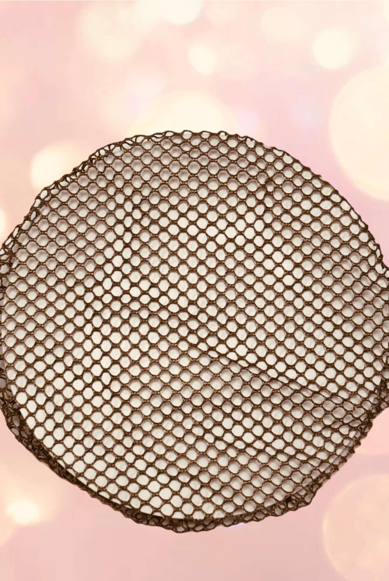 Das Haarnetz Intermezzo 7161 von Intermezzo, ein runder Artikel mit einem sechseckigen Wabenmuster aus dünnem Drahtgeflecht aus 100 % Nylon, steht im Mittelpunkt des Bildes. Der Hintergrund zeigt einen sanften rosa Farbton mit verschwommenen runden Lichtern, die einen Bokeh-Effekt erzeugen.