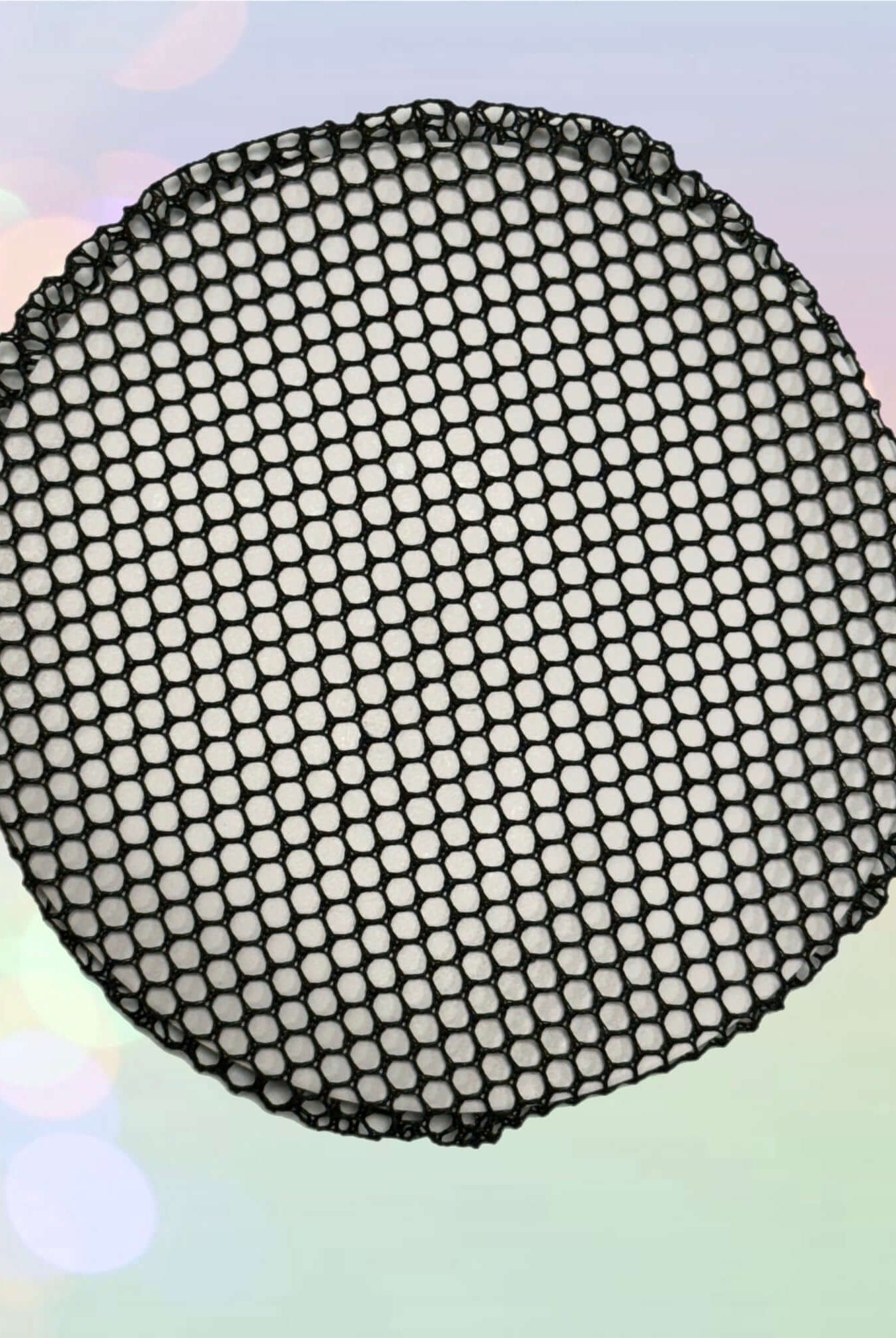 Ein Haarnetz Intermezzo 7161 von Intermezzo, ein rundes, schwarzes, netzartiges Objekt, das an ein Haarnetz erinnert, ist in der Bildmitte vor einem weichen, pastellfarbenen Hintergrund mit leichten Bokeh-Effekten zu sehen. Das robuste Design weist sechseckige Muster auf, die ein netzartiges Aussehen erzeugen, und besteht zu 100 % aus Nylon.