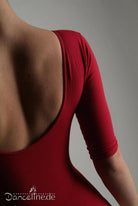 Das Bild zeigt eine Person in einem rückenfreien, roten Ballettanzug APDance 128 Benjamina aus angenehmem Baumwoll-Material. Der Fokus liegt auf dem Rücken und dem rechten Arm der Person. In der unteren linken Ecke erscheint das Logo „Danceline.de“. Der Hintergrund ist schlicht grau.