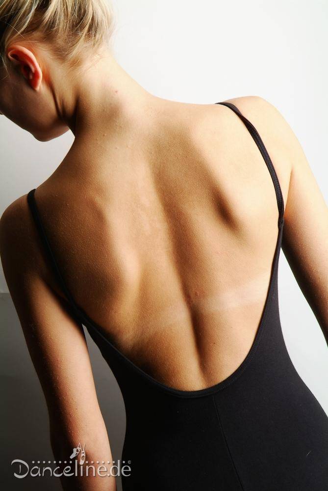 Eine Person mit heller Haut und blondem Haar steht mit dem Rücken zur Kamera. Sie trägt einen Bloch Ballettanzug L5407 Sissone aus Baumwoll-Elasthan-Gemisch. Der schwarze Leotard mit dünnen Trägern legt ihre Rückenmuskulatur frei. In der unteren linken Ecke ist das Logo „Dancelinède“ zu sehen.