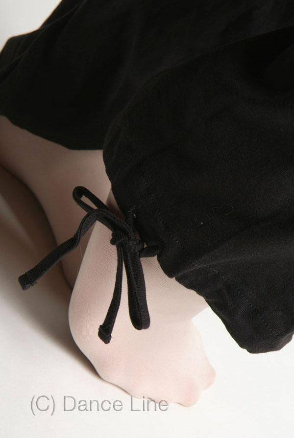 Eine Nahaufnahme der Füße einer Tänzerin in hellen Strumpfhosen, die sich auf das Training vorbereitet. Der Saum der schwarzen Hose, die an einen Bloch Wärmeanzug U1207 Croise erinnert, ist in Knöchelnähe mit einer schwarzen Schnur zusammengebunden. (C) Dance Line.