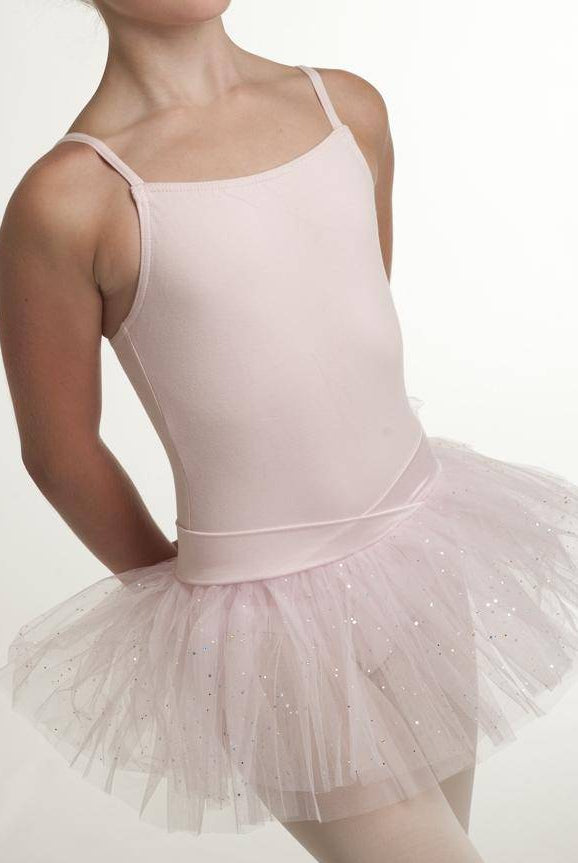 Eine junge Tänzerin ist von den Schultern abwärts zu sehen und trägt einen hellrosa Kinder-Ballettanzug Capezio 9814C Jadica mit Spaghetti-Träger und einen dazu passenden, glitzernden Tüllrock. Die Hände der Tänzerin sind hinter dem Rücken vor einem schlichten weißen Hintergrund positioniert.