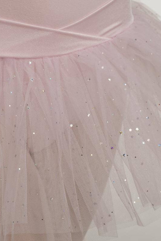 Eine Nahaufnahme des zartrosa Capezio Kinder-Ballettanzugs 9814C Jadica mit einer schimmernden, sternenbesetzten Tüllauflage. Der zarte Stoff des Tüllrocks ist mit kleinen, funkelnden Pailletten verziert, die ihm ein magisches und ätherisches Aussehen verleihen.