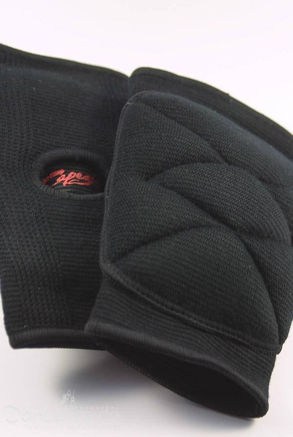 Eine Nahaufnahme eines Paars schwarzer Knieschoner Capezio KP01 Knieschoner. Ein Knieschoner liegt teilweise über dem anderen und zeigt auf der Innenseite ein rotes Logo. Die strukturierte Polsterung sorgt mit einer Öffnung in der Mitte für zusätzlichen Komfort. Der schlichte weiße Hintergrund betont ihr schlankes Design und ihre Bewegungsfreiheit und lässt sie noch deutlicher hervorstechen.