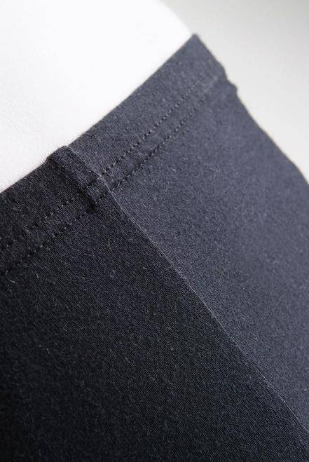 Nahaufnahme einer Person, die schwarze Leggings Danceries G30 Lexie mit hoher Taille von Danceries trägt und eine Hand auf der Hüfte ruht. Nur der untere Rumpf und der obere Oberschenkel sind sichtbar, wodurch der Stoff und die Nahtdetails der Blickdicht-Leggings sichtbar werden.