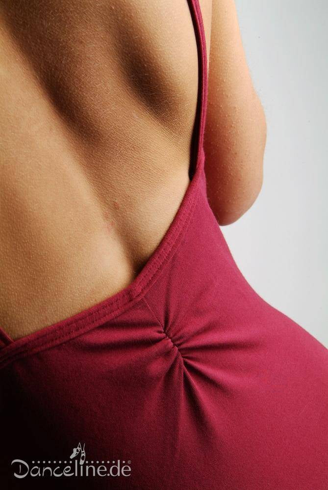 Nahaufnahme des oberen Rückens und der Schultern einer Person, die einen ärmellosen, tiefroten Ballettanzug Danceries T16 Linda mit tiefem Rückenausschnitt trägt. Der Stoff ist am unteren Rücken für zusätzlichen Komfort gerafft. Die Marke „Danceries“ ist in der unteren linken Ecke des Bildes zu sehen und unterstreicht den eleganten Stil.