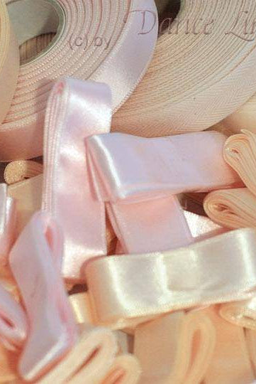 Eine Kollektion hellrosa Sansha Zubehör Spitzenschuhe Bänder DLB Satinis, einige gerollt und einige zu Schleifen gebunden. Das Bild fängt verschiedene sanfte Rosatöne und Texturen ein und zeigt die glänzende, schimmernde Oberfläche des Satinmaterials, das den zarten Charme hervorruft, der mit Spitzenbändern in Tanzzubehör verbunden wird.