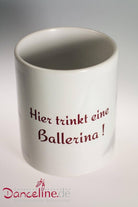 Die Tasse Viscosi T1 Ballerina von Dance Line ist eine weiße Keramiktasse mit der Aufschrift „Hier trinkt eine Ballerina!“ in Rot. Die Ballett-Tasse zeigt außerdem unten rechts ein Logo mit der Aufschrift „Danceline.de - Fachversand für Ballettartikel“ in kleiner roter Schrift, das für gute Laune in Ihrem Tag sorgt.