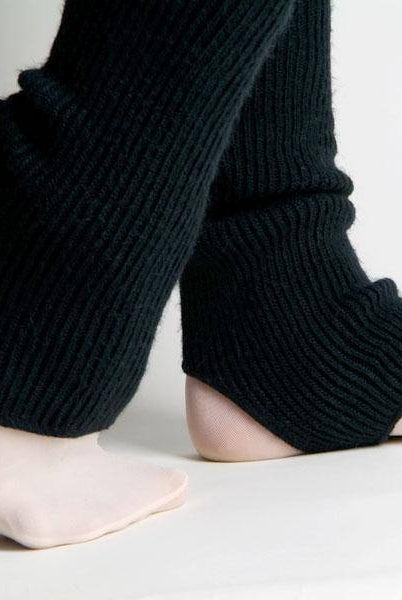 Eine Person, die schwarze Stulpen Intermezzo 2657 Stulpimax von Intermezzo trägt und ihre nackten Füße zeigt, steht auf einer weißen Fläche. Ihre Beine sind übereinandergeschlagen, wobei eine Ferse leicht vom Boden abgehoben ist.