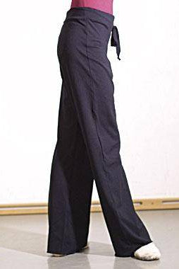 Eine Person trägt die Jazzhose Intermezzo 5894 Bella mit weitem Bein und Kordelzug von Intermezzo und ein rotes Oberteil und hat ein Bein leicht übereinandergeschlagen. Der Hintergrund ist eine schlichte, helle Wand mit hellem Holzboden.