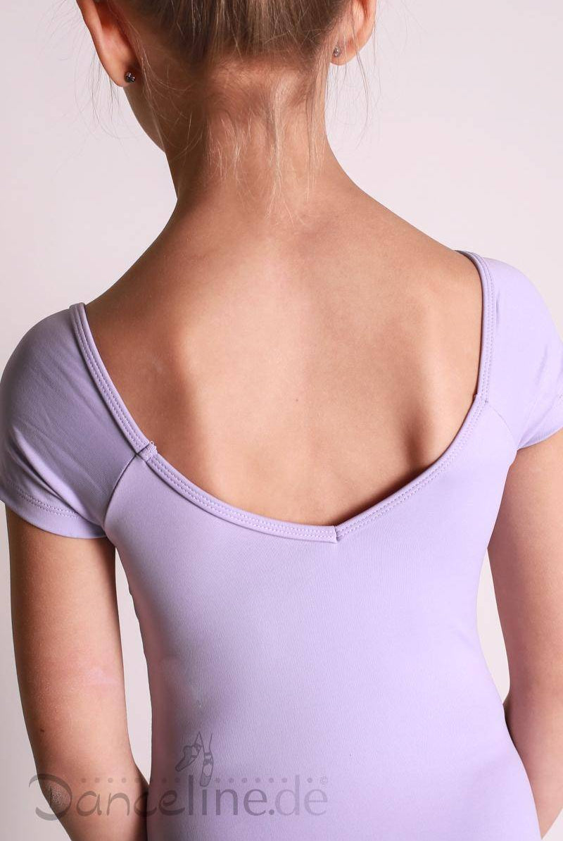 Von hinten ist ein junges Mädchen zu sehen, das einen hellvioletten Dance Line Kinder Ballettanzug Mirella M578C mit Rüschen und Flügelärmeln trägt. Ihr Haar ist zu einem ordentlichen Knoten hochgebunden. Der Hintergrund ist in einer schlichten hellen Farbe gehalten und der untere Teil eines Wasserzeichens mit der Aufschrift „Dandeline.de“ ist sichtbar.