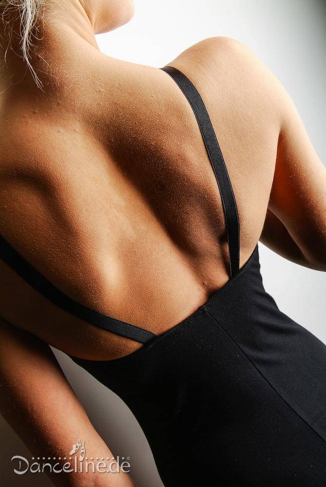 Das Nahaufnahmebild zeigt eine Person von hinten und zeigt den eleganten Ballettanzug RochValley CMajor von Roch Valley. Das schwarze ärmellose Kleid hat zarte Spaghetti-Träger, die über den Schultern verlaufen und die gut definierten Muskeln des oberen Rückens und der Schultern betonen. Das Danceline.de-Logo ist in der unteren linken Ecke sichtbar.