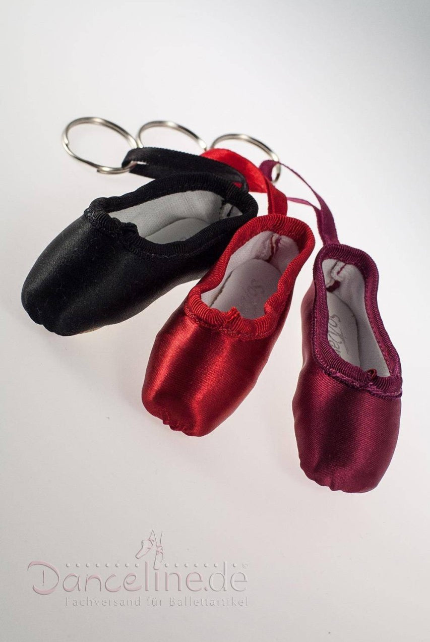 Drei Miniatur-Ballettschuh-Schlüsselanhänger von SoDanca, genannt Mini-Spitzenschuh-Anhänger SoDanca KCE01 Minipoint, sind in schwarzem, rotem und burgunderfarbenem Satin erhältlich. Diese Mini-Spitzenschuhe haben zur praktischen Verwendung Metallringe. Vor einem weißen Hintergrund sind das Logo und der Text „Danceline.de“ unten teilweise sichtbar – perfekt als Geschenk!