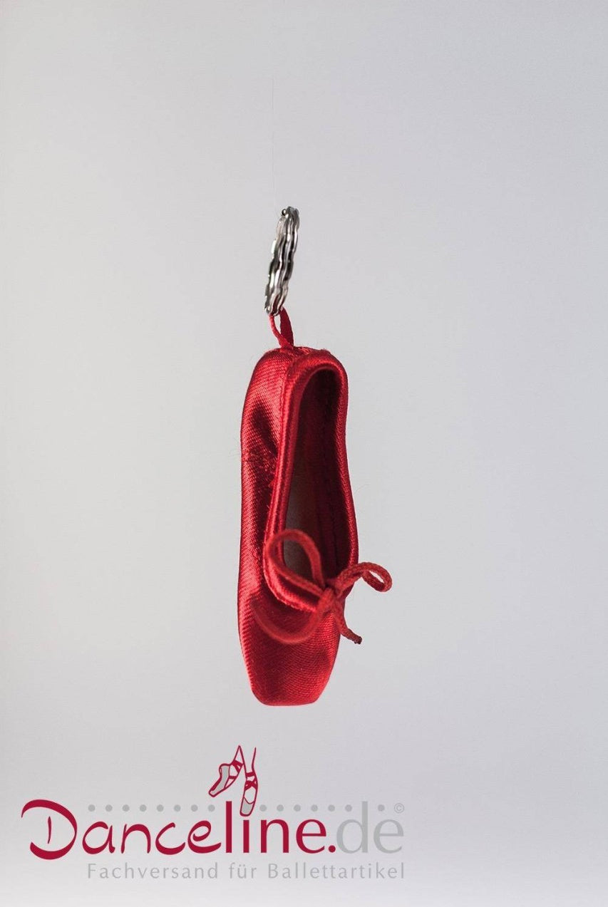 Ein kleiner, roter Ballettschuh-Schlüsselanhänger von Sansha hängt vor einem schlichten weißen Hintergrund. Der Mini-Spitzenschuh-Anhänger Sansha KRPS Minipoint zeigt einen Mini-Ballettschuh aus glänzendem rotem Stoff. Unter dem Schuh steht der Text „Danceline.de Fachversand für Ballettartikel“.