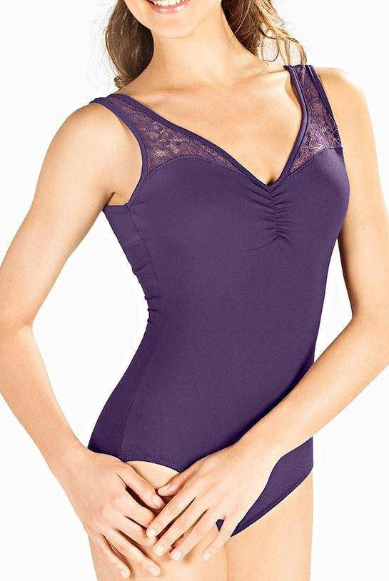 Eine Frau trägt den SoDanca Ballettanzug E10910 Melanie, einen violetten ärmellosen Ballettanzug mit elastischer Spitze am Ausschnitt, und steht mit locker vor sich gefalteten Händen vor einem schlichten weißen Hintergrund.