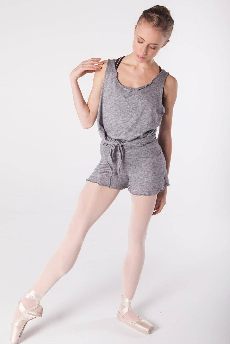 Eine Tänzerin trägt einen grauen Leotard mit passendem Gürtel, weiße Strumpfhosen und rosa Ballettschuhe und nimmt eine selbstbewusste Ballettpose mit leicht zur Seite geneigtem Kopf ein. Ihr Outfit umfasst unter dem Leotard die Hose Intermezzo 5213 Nacurt von Intermezzo für zusätzlichen Komfort. Der Hintergrund ist schlicht weiß.