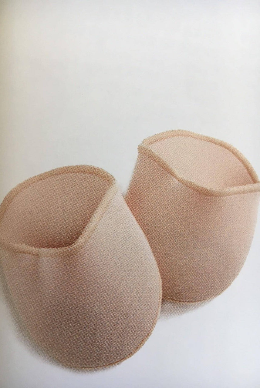 Zwei hellrosa, halbrunde Zehenpolster aus Stoff, bekannt als Zehenpolster Bunhead BH005 OuchPouch von Dance Line, sind nebeneinander vor einem weißen Hintergrund platziert. Jedes Polster ist an einem Ende offen und scheint gepolstert zu sein, wahrscheinlich für den Einsatz in Tanzschuhen für zusätzlichen Komfort und Schutz konzipiert.