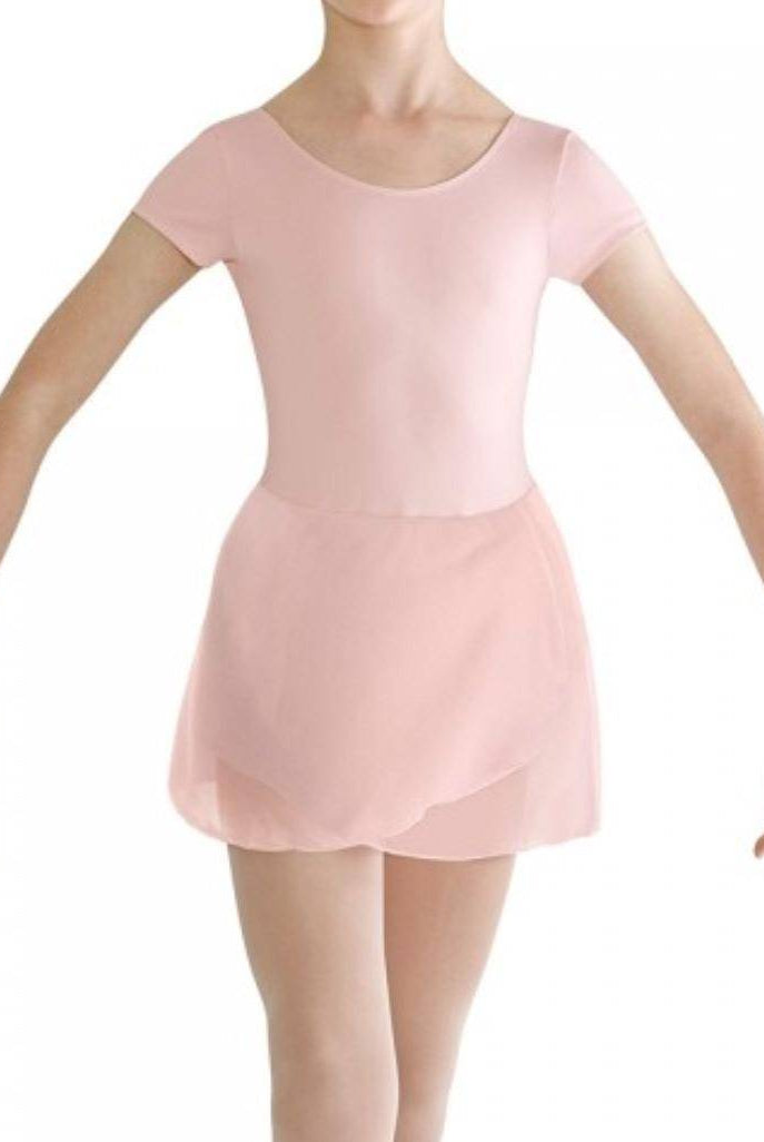 Eine Balletttänzerin in einem hellrosa Bloch Kinder Ballettanzug CL8262 Prisha mit einem Georgette Rock posiert mit anmutig zur Seite ausgestreckten Armen. Das Gesicht der Tänzerin ist nicht sichtbar. Der Hintergrund ist schlicht, sodass der Fokus auf die elegante Figur der Tänzerin gerichtet ist.