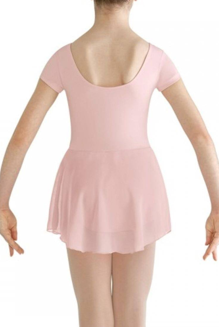 Eine junge Person ist von hinten abgebildet und trägt den Bloch Kinder Ballettanzug CL8262 Prisha in Hellrosa. Das Outfit besteht aus einem Turnanzug mit Flügelärmeln und U-Ausschnitt sowie einem transparenten Georgette-Rock. Die Person steht vor einem schlichten weißen Hintergrund mit leicht ausgestreckten Armen an den Seiten.