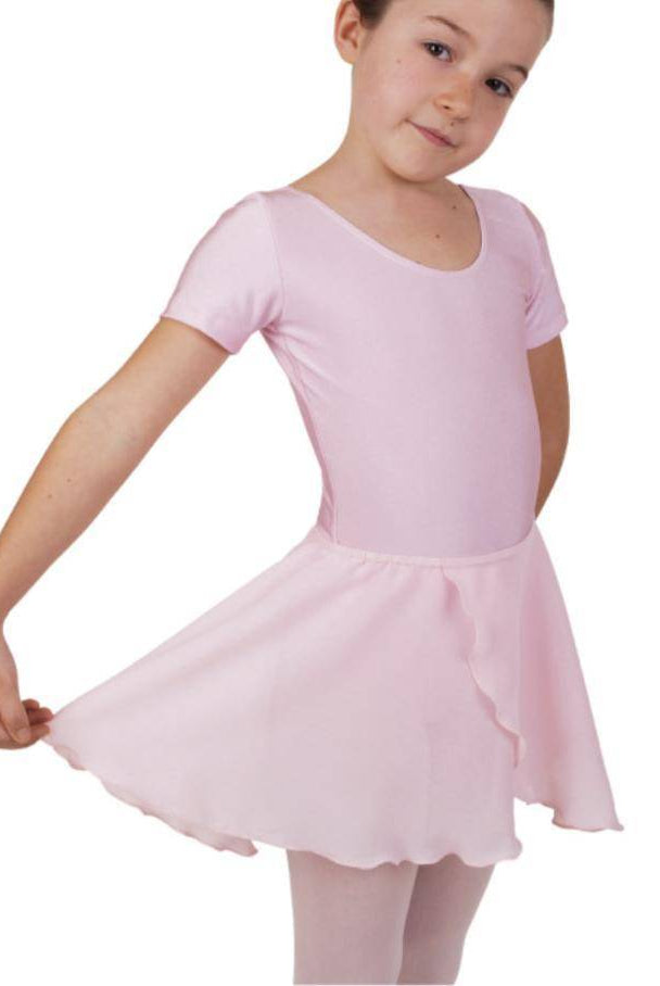 Ein junges Mädchen steht in einem rosa Ballett-Outfit und hält die Ränder ihres Rocks in Wickeloptik Danceries Z39 Lilly von Danceries seitlich nach außen. Sie scheint anmutig zu posieren, mit einem leichten Lächeln und dem Kopf zur Seite geneigt. Sie hat kurze Haare und sieht in ihrem zarten Ensemble aus Georgette-Stoff so aus, als wäre sie bereit für eine Tanzvorführung oder eine Übung.