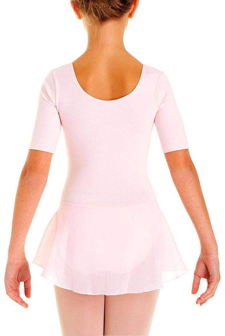 Ein junges Mädchen steht mit abgewandtem Gesicht da und trägt einen hellrosa Intermezzo Kinder Ballettanzug 3058 mit kurzen Ärmeln und einem fließenden Rock. Ihr Haar ist zurückgebunden und ihre Arme hängen entspannt an den Seiten. Sie scheint in einer neutralen Position zu stehen und erinnert mit zarten Prinzessinnen-Nähten an die Anmut von Intermezzo.