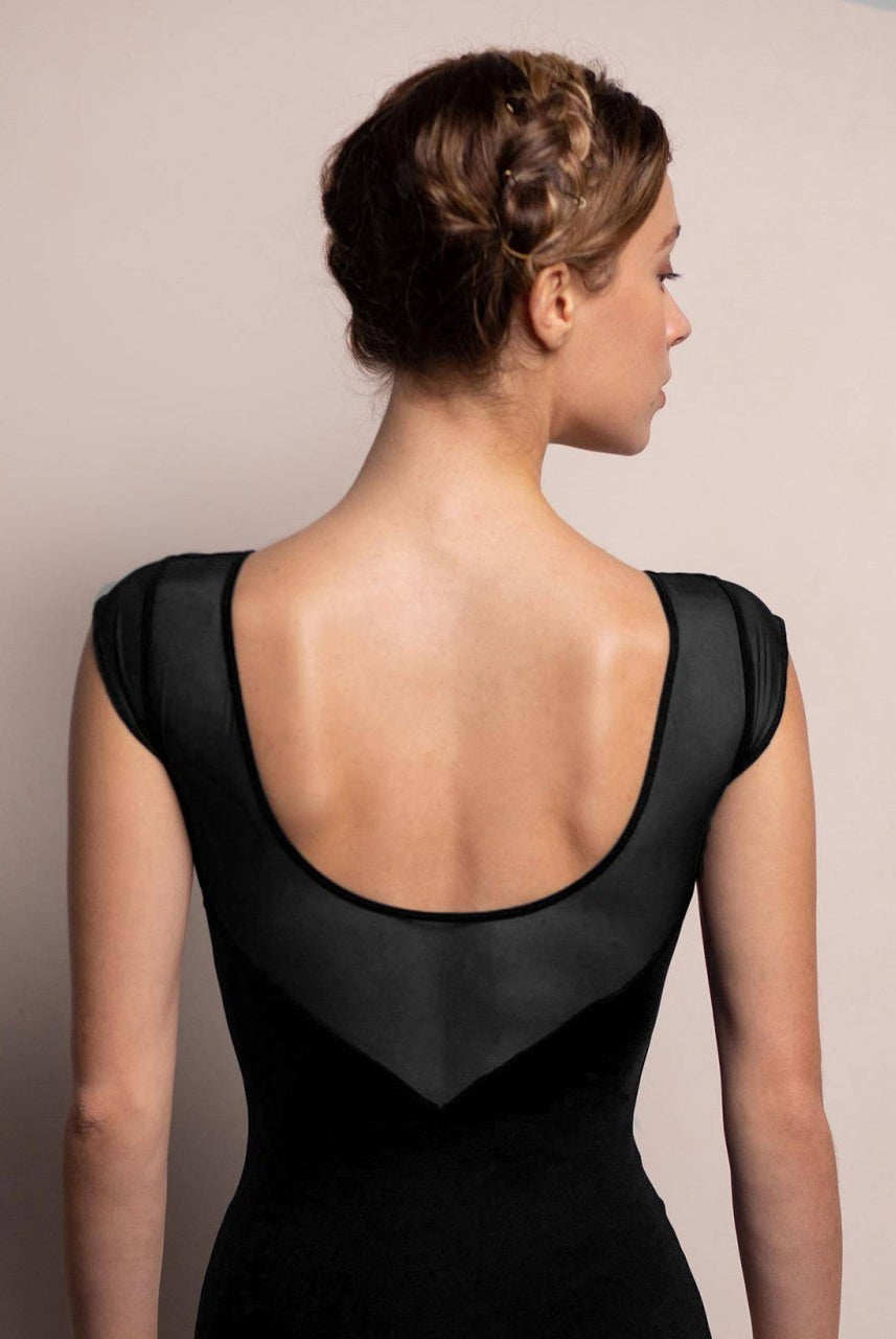 Eine Frau mit geflochtenen braunen Haaren ist von hinten zu sehen. Sie trägt den Intermezzo Ballettanzug 31547 Mesh, ein schwarzes Kleid mit tiefem Rückenausschnitt und zarten Netzdetails. Sie steht vor einem einfachen zweifarbigen Hintergrund in neutralen Farben.