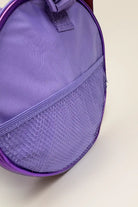 Eine Detailansicht der Balletttasche Capezio Cosmo B277 von Capezio zeigt eine glänzende, violette, runde Tasche mit einer Netztasche auf der Vorderseite. Sie ist auf einem schlichten, hellbeigen Hintergrund platziert.