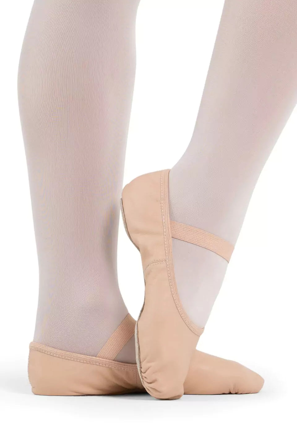 Eine Person in weißer Strumpfhose und den Capezio Ballettschuhen V100 Luna in Beige steht in einer Ballettpose vor einem schlichten Hintergrund. Die Schuhe haben oben elastische Riemen.