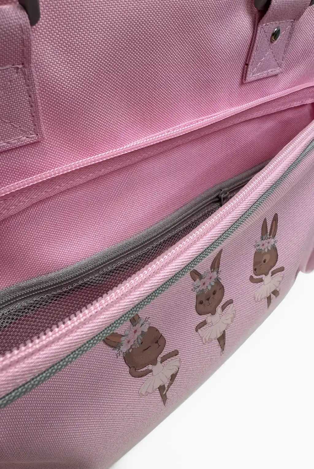 Eine Nahaufnahme der Kinder-Balletttasche Danceline Ballet Bears von Danceline, die drei Cartoon-Balletttänzer-Häschen mit Blumenkronen und Tutus auf einer rosa Stofftasche zeigt. Das Bild hebt eine offene Reißverschlusstasche an der Tasche hervor.