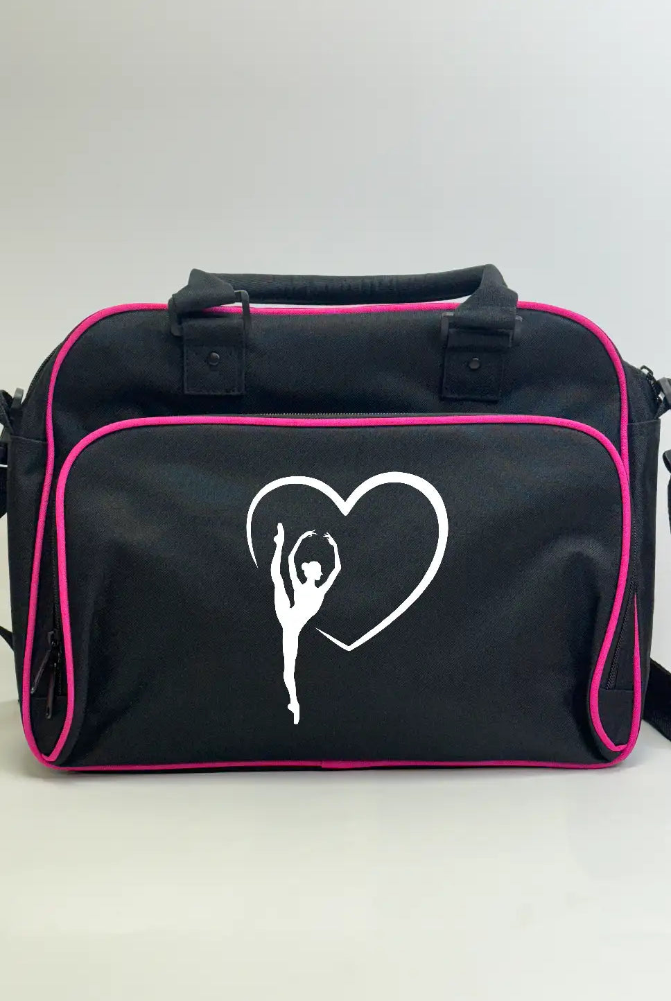 Wir präsentieren die Balletttasche Danceline Herz-Ballett von Danceline: eine stilvolle schwarze Reisetasche mit elegantem rosa Rand, verziert mit der weißen Silhouette einer Ballerina, die ihre Arme anmutig vor einem Herzumriss ausstreckt. Diese vielseitige Tasche verfügt über zwei praktische kurze Griffe und einen abnehmbaren Schultergurt für müheloses Tragen.