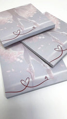 Piles of Block Danceline-Notizbücher „Dancing around“ von Dance Line mit einem Ballettthema in sanften Rosa- und Weißtönen. Das Coverdesign hebt Ballettschuhe und eine durchgehende rote Linie hervor, die in der Ecke eine Herzform bildet.