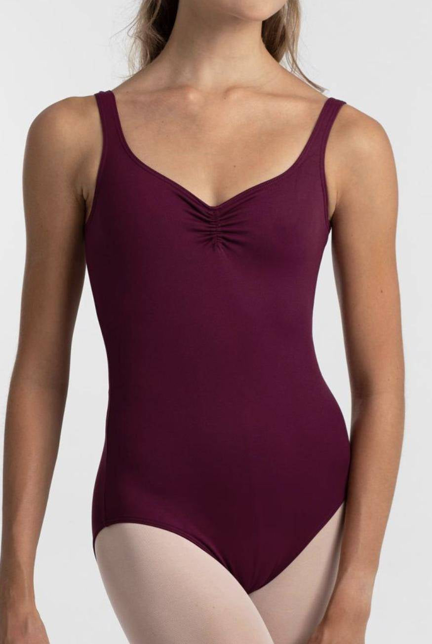 Eine Person trägt einen ärmellosen, kastanienbraunen Ballettanzug Intermezzo 31232 Marya von Intermezzo mit hochwertigen Details und einer gerafften Vorderseite. Der Ballettanzug scheint aus schnelltrocknendem Material zu sein. Die Person trägt darunter außerdem helle Strumpfhosen. Der Hintergrund ist schlicht weiß.