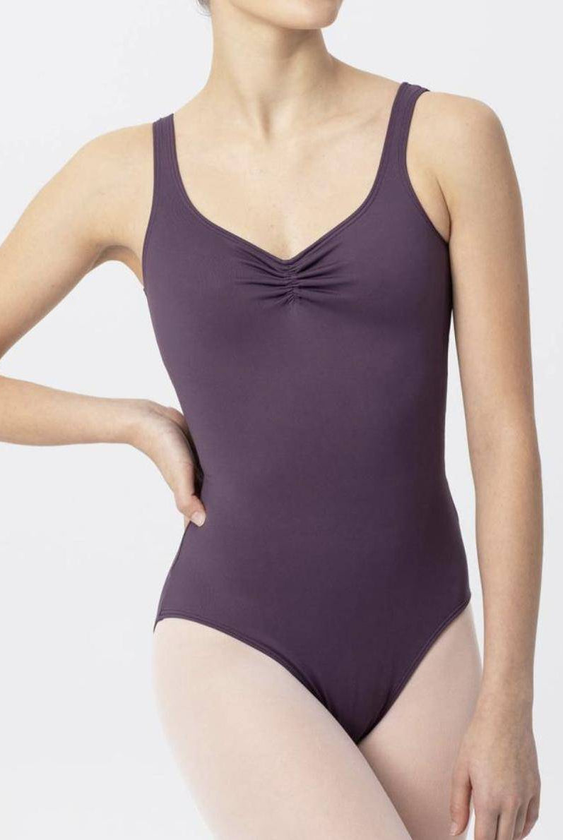 Eine Person in einem dunkelvioletten, ärmellosen Ballettanzug Intermezzo 31232 Marya von Intermezzo, aus schnelltrocknendem Material, posiert mit einer Hand auf der Hüfte vor einem schlichten Hintergrund. Der Ballettanzug weist dezente, hochwertige Details auf, darunter gerüschte Details am Ausschnitt.