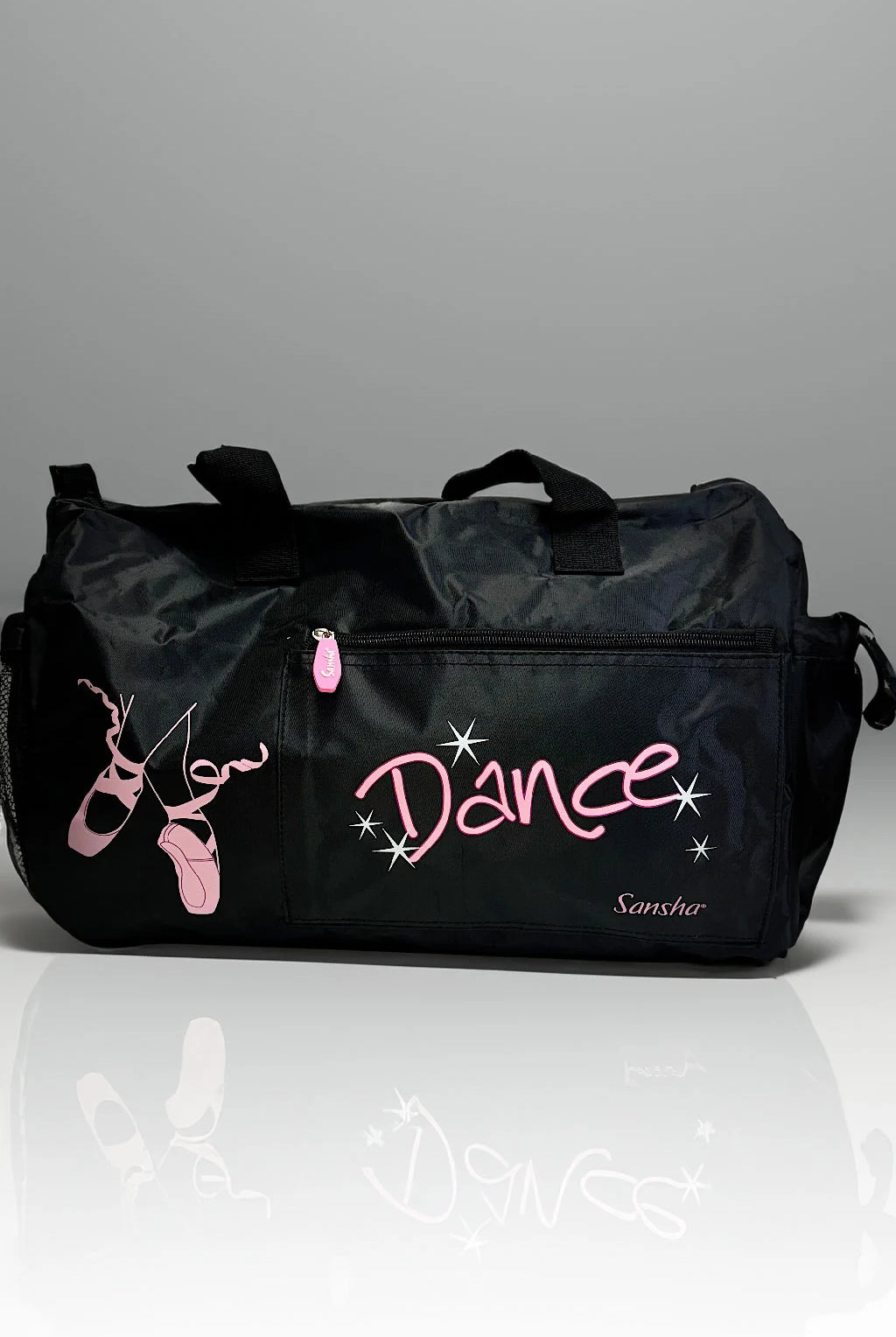 Die Dance Line Balletttasche Sansha KBAG2 ist eine elegante schwarze Tanztasche, die mit einer rosa Ballettschuhillustration und dem Wort „Dance“ in Rosa auf der Seite verziert ist. Sie verfügt über eine Vordertasche mit Reißverschluss und zwei Tragegriffe oben, die sich alle schön vor einem grauen Hintergrund mit einer reflektierenden Oberfläche darunter präsentieren.