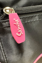 Eine Nahaufnahme der Dance Line Balletttasche Sansha KBAG2 zeigt ihren glänzenden Stoff und ihr schwarzes Taschendesign, akzentuiert durch einen rosa Reißverschluss mit der Prägung „Sansha“.