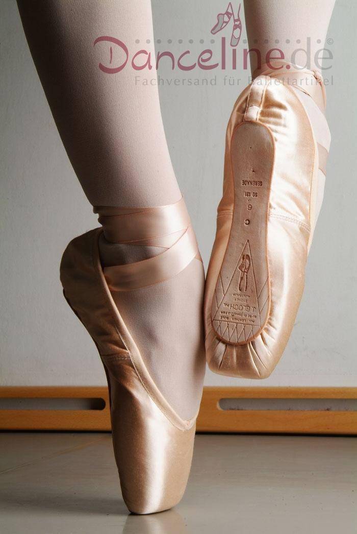 Nahaufnahme der Füße einer Balletttänzerin in rosa Bloch Spitzenschuhen S0131S Serenade Strong, die auf Zehenspitzen steht. Das Danceline.de-Logo und der Text „Fachversand für Ballettartikel“ sind oben im Bild zu sehen. Im Hintergrund sind außerdem die weißen Strumpfhosen der Tänzerin und eine hölzerne Ballettstange zu sehen.