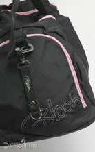 Eine Nahaufnahme der Ballett Tasche Bloch A311 Duffle in Schwarz mit rosa Akzenten und silberfarbener Hardware. Der Markenname „Bloch“ ist in Pink auf die Vordertasche gestickt. In der Nähe des Reißverschlusses ist ein Logo-Tag mit einem Metallclip angebracht. Der Hintergrund ist weiß.