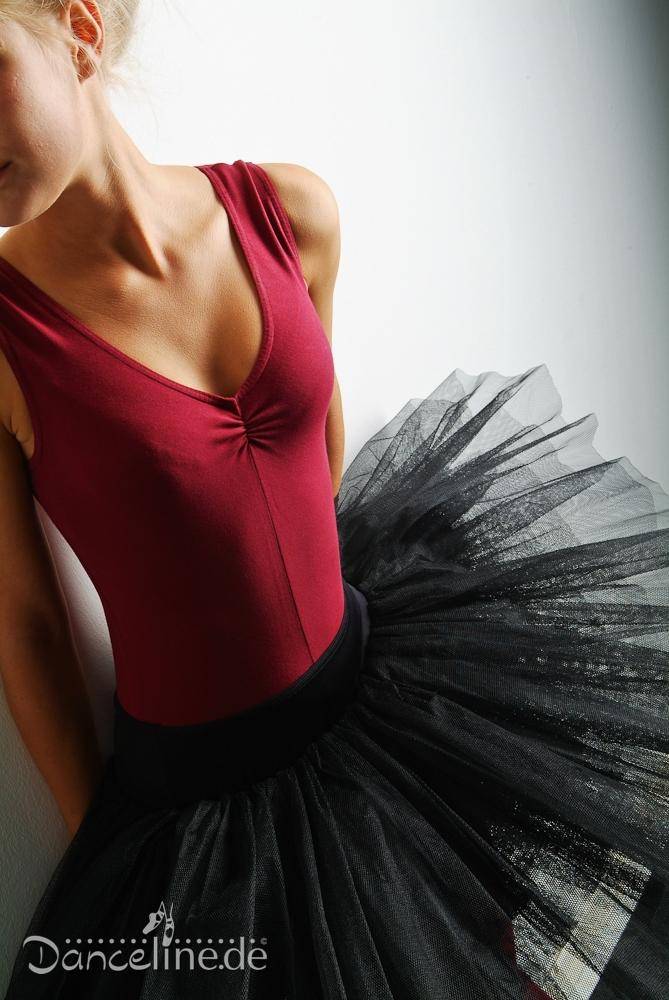 Eine Tänzerin in einem burgunderfarbenen Leotard und einer schwarzen Tutulette Bloch R2921 Belle von Bloch steht vor einer weißen Wand. Das Foto zeigt ihren Oberkörper und das Tutu in Nahaufnahme, wobei ihr Gesicht teilweise außerhalb des Bildes liegt. Unten ist das Logo „Danceline.de“ zu sehen.