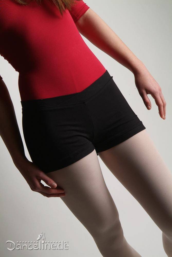 Eine Person, die einen roten Turnanzug mit V-Ausschnitt, die schwarze Hose Bloch R3614 Pantie Hotpants und weiße Strumpfhosen trägt, steht mit leicht nach unten gestreckten Armen da. Das Bild ist so zugeschnitten, dass der Körper von der Schulter bis zu den Oberschenkeln zu sehen ist. Der Hintergrund ist schlicht weiß.