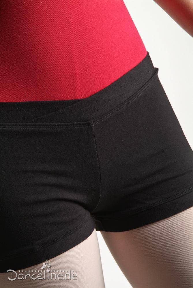 Nahaufnahme einer Person, die ein rotes V-Ausschnitt-Oberteil und die schwarze hoch taillierte Hose Bloch R3614 Pantie von Bloch trägt, die den Bauch und die oberen Oberschenkel zeigt. Das Foto hebt die Kleidungsdetails und die Passform hervor und betont den auffälligen Kontrast zwischen den roten und schwarzen Stoffen.