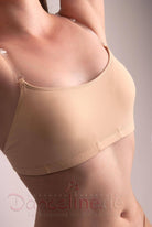 Eine Person ist vom Hals bis zur Taille zu sehen und trägt ein hautfarbenes Capezio BH Capezio 3564 Layana Camisole Bra Top mit transparenten Trägern. Der Hintergrund ist einfarbig. Am unteren Bildrand sind in roter Schrift das Wort „Danceline.de“ und der Satz „Fachversand für Ballettartikel“ zu sehen.