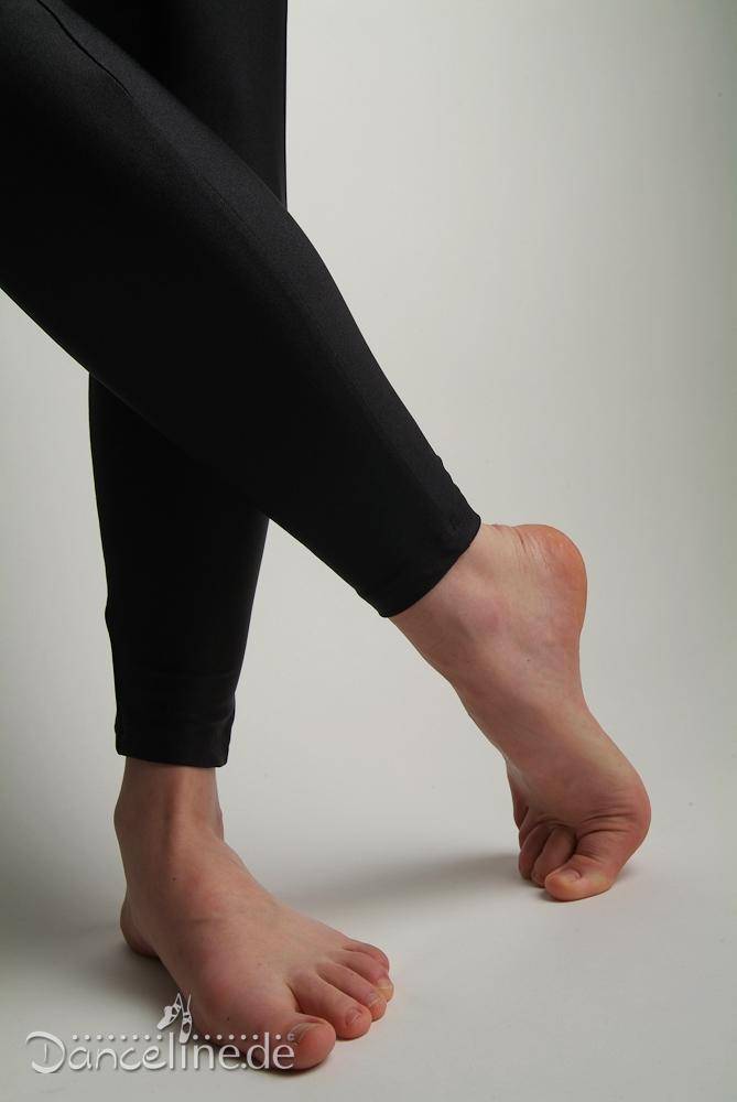 Eine Person in schwarzen Leggings und einem eleganten Ganzanzug Danceries G16L Gwenny EL steht auf einem Bein, wobei der andere Fuß angehoben und nach unten gerichtet ist, was eine Tanzpose suggeriert. Der Hintergrund ist schlicht weiß und das Bild konzentriert sich deutlich auf die Füße und Unterschenkel. Das Logo „Danceline.de“ ist unten sichtbar.