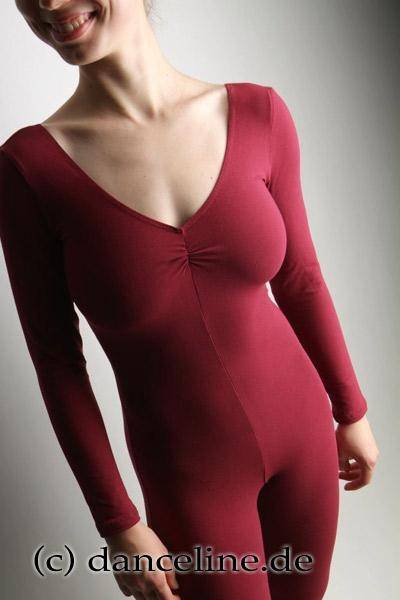 Person trägt einen roten, langärmeligen Ganzanzug Danceries G21 Nora mit Raffung im Ausschnitt und posiert mit einem leichten Lächeln. Das Foto ist von links schräg aufgenommen und fokussiert auf den Oberkörper. Der Hintergrund ist schlicht und hell. Am unteren Bildrand ist „c) danceline.de“ eingeprägt.