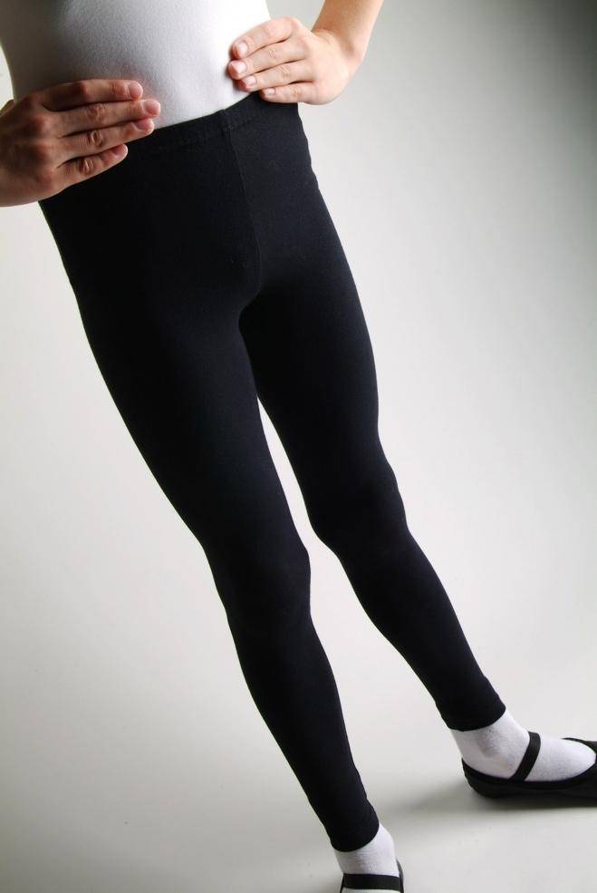 Eine Person, die die Hose Danceries G30 Lexie Leggings in Schwarz, weiße Socken und schwarze Ballettschuhe trägt, steht mit einer Hand auf der Hüfte vor einem neutralen Hintergrund. Das Bild konzentriert sich auf die Beine und einen Teil des Oberkörpers und suggeriert einen Ballett- oder Tanzkontext aus der Danceries-Kollektion.