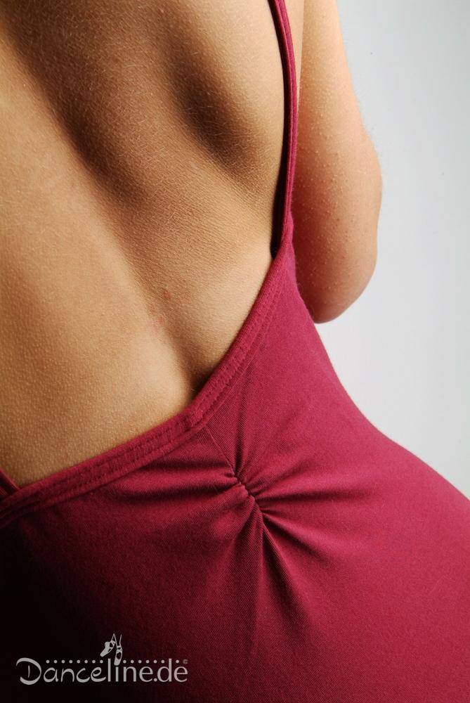 Nahaufnahme des oberen Rückens und der Schultern einer Person, die einen ärmellosen, tiefroten Ballettanzug Danceries T16 Linda mit tiefem Rückenausschnitt trägt. Der Stoff ist am unteren Rücken für zusätzlichen Komfort gerafft. Die Marke „Danceries“ ist in der unteren linken Ecke des Bildes zu sehen und unterstreicht den eleganten Stil.
