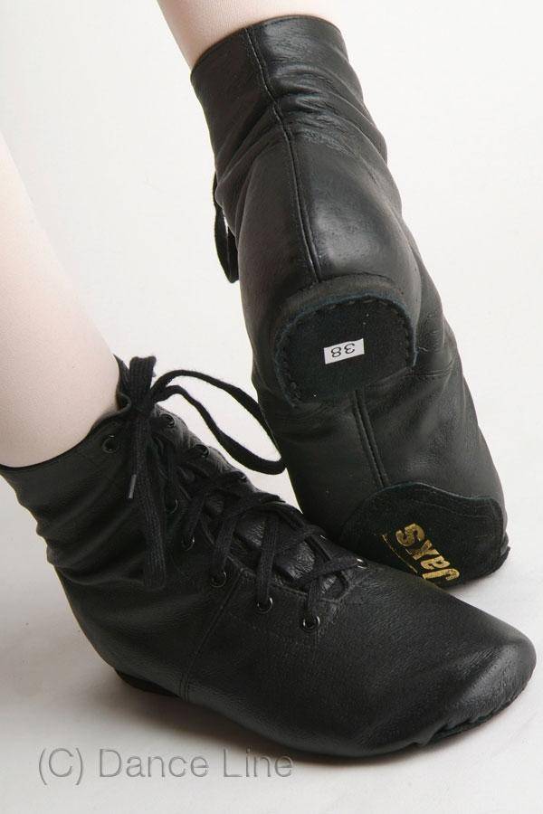 Nahaufnahme eines Paars Füße, die Dance Line Jazzschuhe Jaxs Boots in Schwarz tragen, fest geschnürt. Die Stiefel haben ein Etikett mit der Größe 38, ein Logo auf der Ferse und eine geteilte Chromledersohle. Die Person steht auf den Zehen, was das spitzenschuhähnliche Design der robusten Lederstiefel hervorhebt. Der Text lautet „(C) Dance Line.