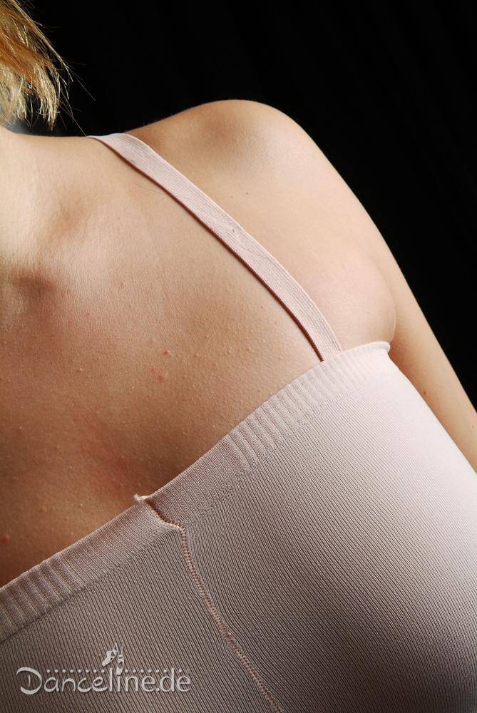Nahaufnahme einer Person, die ein hellrosa Spaghettiträgertop trägt, das an die Ballettstrumpfhose Rumpf 110 Complete von Rumpf erinnert, wobei der Fokus auf Schulter und oberem Rücken liegt. Die Stoffstruktur und die Nähte sind sichtbar, während der dunkle Hintergrund den Kontrast verstärkt. Das Wort „Dancelinede“ ist unten teilweise sichtbar.