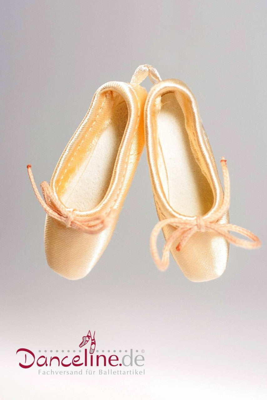 Eine Nahaufnahme eines cremefarbenen Mini-Spitzenschuh-Paares Sansha MPS Empees mit hellrosa Schleifen. Die Ballettschuhe, die Mini-Spitzenschuhen ähneln, hängen an ihren Bändern in der Luft, vor einem schlichten weißen Hintergrund. Unten ist das Logo „Danceline.de Fachversand für Ballettartikel“ zu sehen.