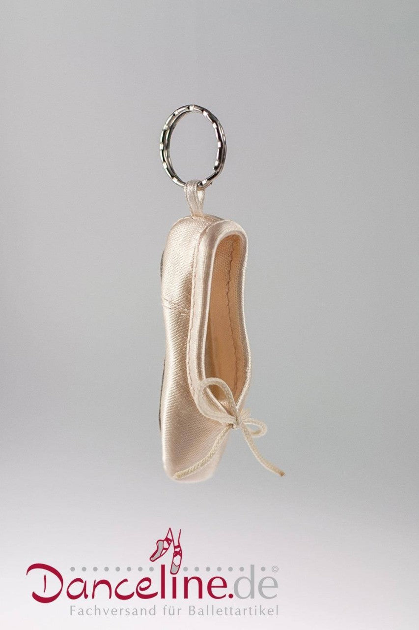 Ein Schlüsselanhänger mit dem Mini-Spitzenschuh-Anhänger Sansha KRPS Minipoint mit feiner Stickerei und einer kleinen Schleife auf der Vorderseite. Der Schlüsselanhänger ist an der Ferse des Schuhs befestigt. Am unteren Bildrand sind das Logo „Danceline.de“ und der Slogan „Fachversand für Ballettartikel“ zu sehen.